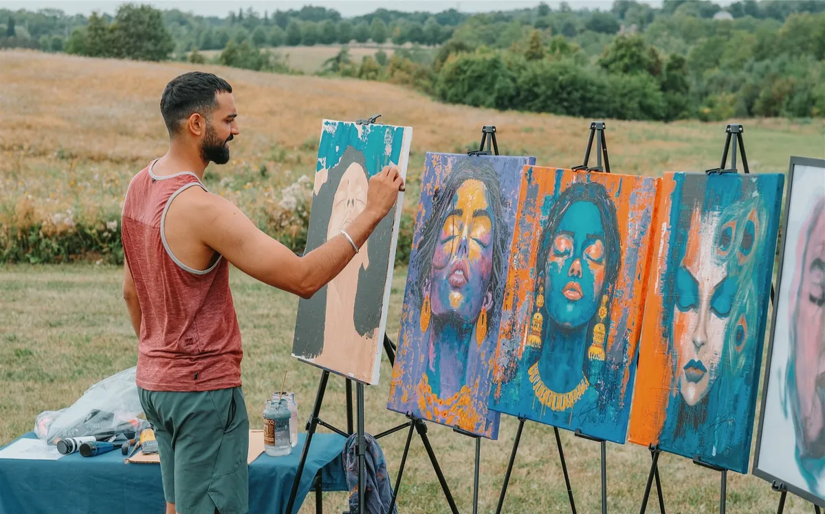 Amit Tejpal painting live at an outdoor festival beside a row of his acrylic portraits